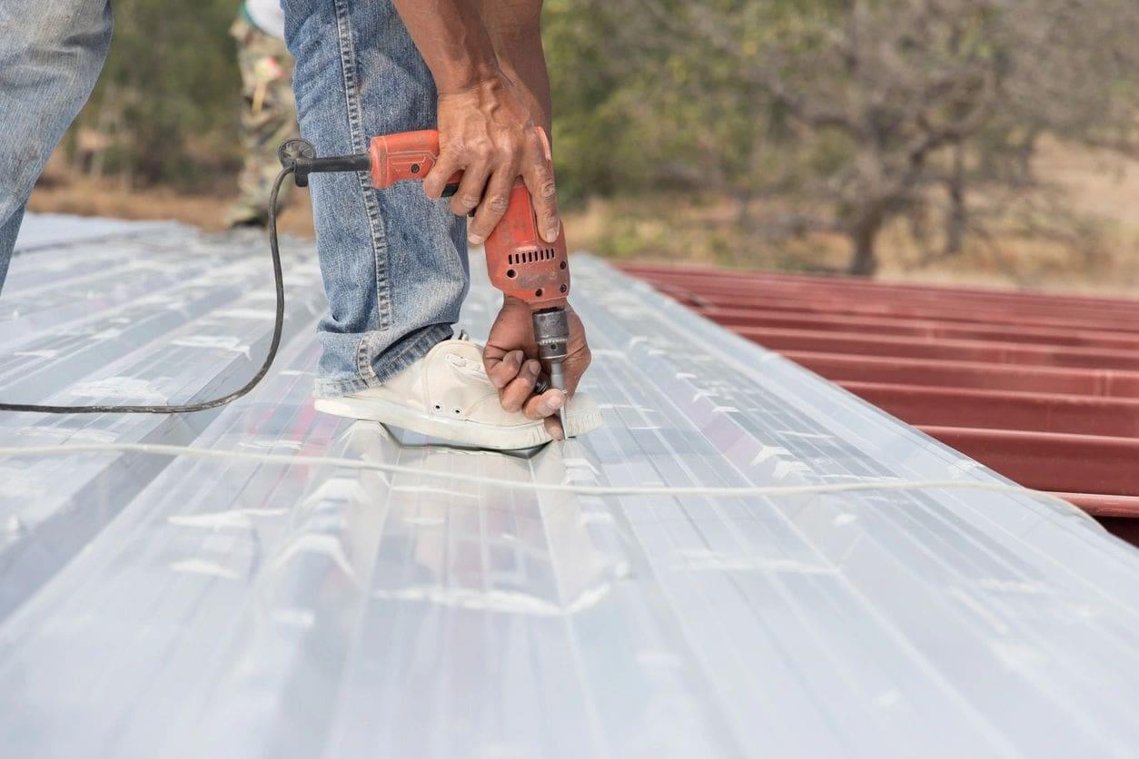Man drilling metal roof with drill.