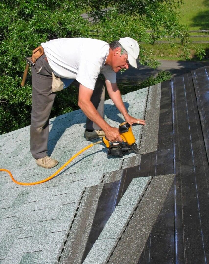 Roofer installing shingles with nail gun.